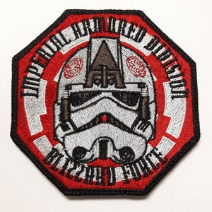 May include: A red and white embroidered patch with a white stormtrooper helmet in the center. The text around the helmet reads "Imperial Armored Division Blizzard Force".