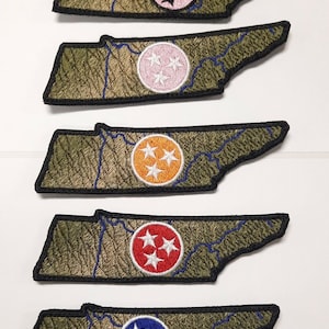 Könnte beinhalten: Fünf gestickte Aufnäher des Bundesstaates Tennessee mit unterschiedlichfarbigen Kreisen und weißen Sternen in der Mitte. Die Aufnäher befinden sich auf weißem Hintergrund.