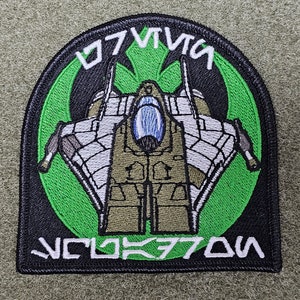 May include: A black and green embroidered patch featuring a spaceship with the text "V77-VI" and "VCL3K770V" in white.