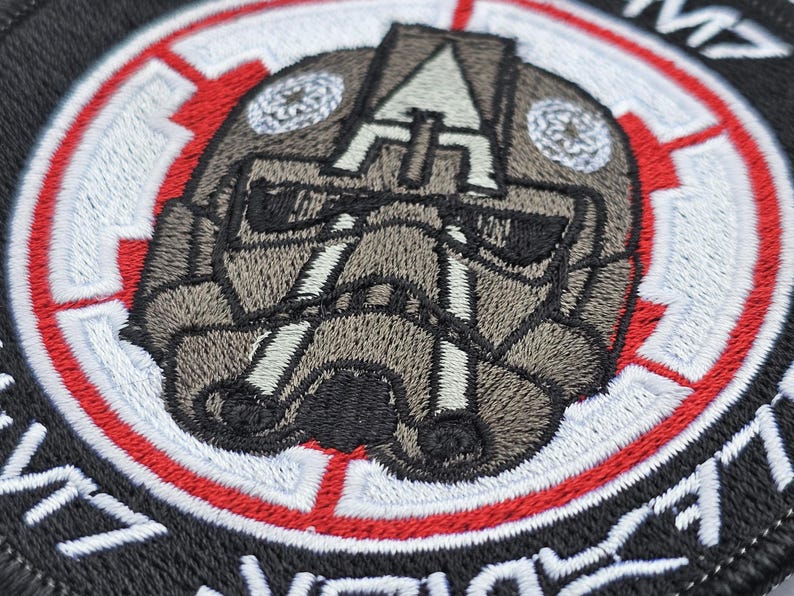 May include: A black and white embroidered patch with a red and white circle around a gray and white helmet design. The text "71st  Infantry Division" is embroidered around the outside of the patch.