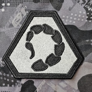 Op de afbeelding: Een geborduurde patch in zwart en wit met een schorpioenontwerp in een zeshoekige vorm.