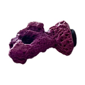 Puede incluir: Decoración de coral artificial morado texturizado con un agujero oscuro y una base negra. El coral tiene una superficie porosa y está diseñado para uso en acuarios. La pieza decorativa es una adición vibrante a cualquier escena submarina.