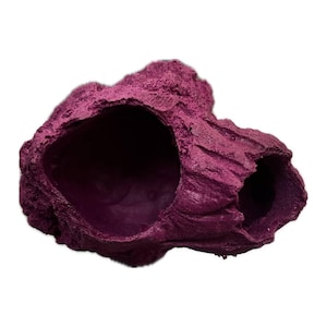 May include: A deep magenta, rock-like aquarium ornament featuring two distinct, hollowed-out openings with a rough, textured exterior surface. The structure has an irregular, organic shape with a dark interior visible through the two cavities.