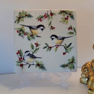 May include: A white ceramic tile with a wintery design featuring three birds, holly leaves, and red berries.