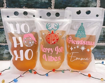 May include: Three clear plastic pouches with festive Christmas designs and text. The pouches are filled with a brown liquid and have a zipper closure. The text on the pouches reads "Ho Ho Ho", "Merry Jolly Vibes", and "Friendsmas Emma".