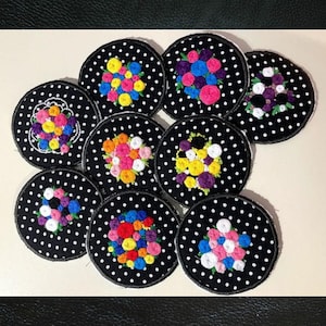 Può includere: Nove cerchi di tessuto ricamati con pois neri e mazzi di fiori colorati. Ogni cerchio ha uno schema di colori e una disposizione dei fiori diversi.