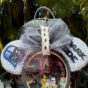May include: Black backpack with a clear front, showcasing Star Wars pins. The backpack features a black and white bow, and mouse ears with "Dark Side" text and a blue and purple design. A black headband is visible.