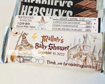 May include: A white chocolate bar wrapper with a Harry Potter themed design. The wrapper features a Hogwarts castle, a witch's hat, a lightning bolt, and the text "Malloty's Baby Shower September 10, 2023".