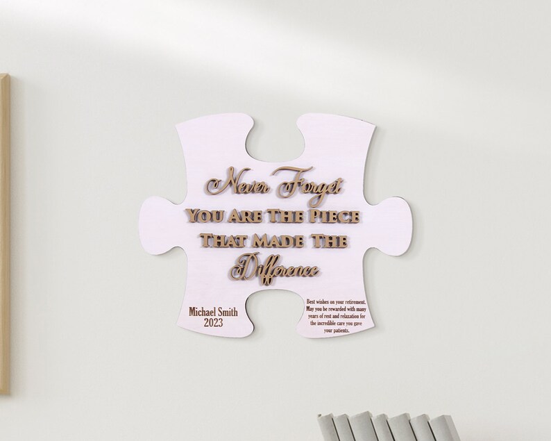 Peut inclure: Une pi&egrave;ce de puzzle en bois blanc avec le texte "Never Forget You Are The Piece That Made The Difference" et le nom "Michael Smith" et l'ann&eacute;e "2023".