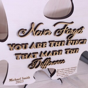 Peut inclure: Pi&egrave;ce de puzzle en bois blanc avec le texte "Never Forget You Are The Piece That Made The Difference" en lettres dor&eacute;es. Le texte "Michael Smith 2023" est grav&eacute; au bas de la pi&egrave;ce.