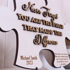 Peut inclure: Une pi&egrave;ce de puzzle en bois en forme de puzzle avec le texte "Never Forget You Are The Piece That Made The Difference" en lettres dor&eacute;es. Le texte "Michael Smith 2023" est &eacute;galement inclus dans le coin inf&eacute;rieur droit.