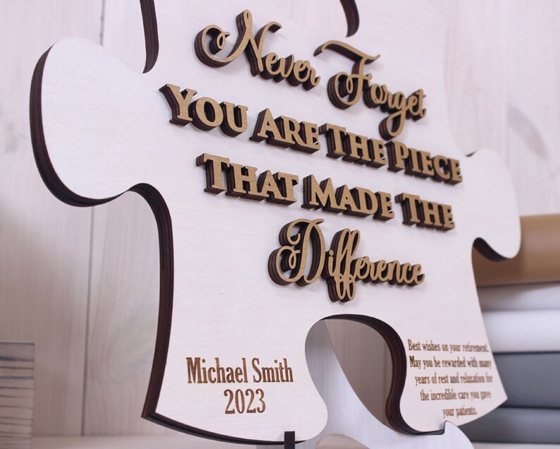 Peut inclure: Une pi&egrave;ce de puzzle en bois en forme de puzzle avec le texte "Never Forget You Are The Piece That Made The Difference" en lettres dor&eacute;es. Le texte "Michael Smith 2023" est &eacute;galement inclus dans le coin inf&eacute;rieur droit.