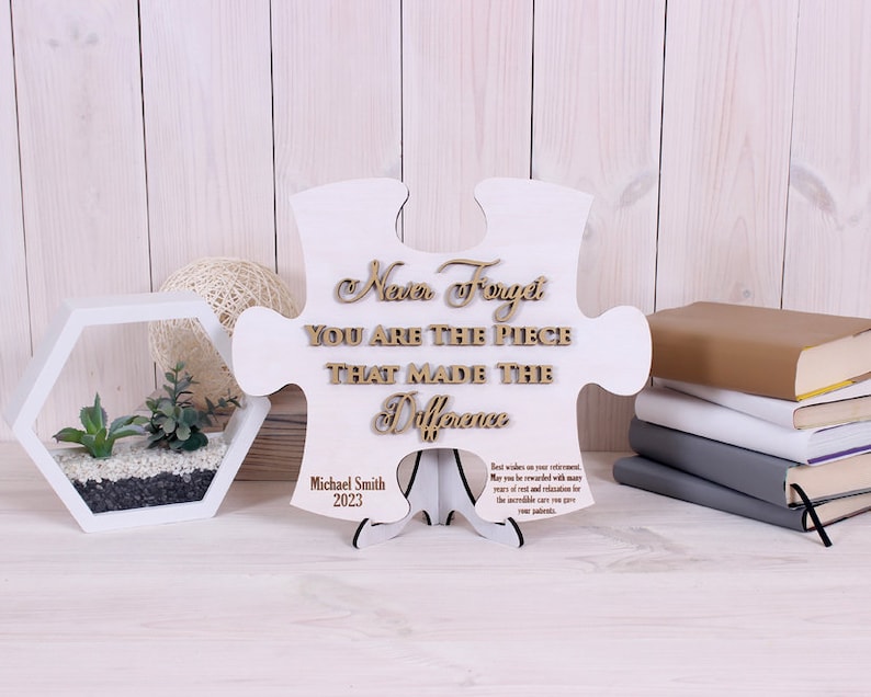 Peut inclure: Une pi&egrave;ce de puzzle en bois blanc en forme de puzzle avec les mots "Never Forget You Are The Piece That Made The Difference" en lettres brunes. Le bas de la pi&egrave;ce porte le nom "Michael Smith" et l'ann&eacute;e "2023" en lettres noires.
