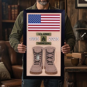 May include: Framed wooden artwork featuring an American flag, U.S. Army insignia, service years, and name. Below are detailed illustrations of combat boots. The artwork is held by a person.