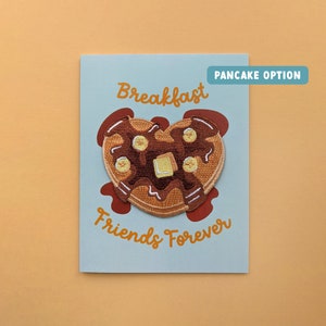 May include: A light blue card with the text "Breakfast Friends Forever" in orange. A heart-shaped pancake with chocolate syrup and banana slices is embroidered on the card. The text "Pancake Option" is in a blue box in the top right corner.