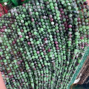 Könnte beinhalten: Nahaufnahme von Strängen aus facettierten Edelsteinperlen in Grün, Dunkelgrau und Burgunderrot. Die kleinen Perlen sind aufgereiht und bilden eine strukturierte und farbenfrohe Darstellung. Diese Perlen werden wahrscheinlich für die Schmuckherstellung verwendet.