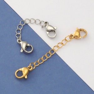 Peut inclure: Deux rallonges de chaîne argentées et dorées avec des fermoirs à ressort. Les rallonges sont sur un fond blanc et bleu.