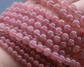 Könnte beinhalten: Eine Schnur aus rosafarbenen Quarzperlen, jede Perle ist rund und durchscheinend mit einem leichten Glitzern. Die Perlen sind auf einem dünnen roten Faden aufgefädelt.