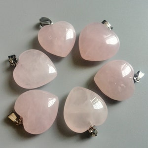 May include: Six pink heart-shaped rose quartz pendants with silver bail loops. The pendants are arranged in a circle on a light gray background.