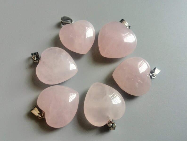 May include: Six pink heart-shaped rose quartz pendants with silver bail loops. The pendants are arranged in a circle on a light gray background.