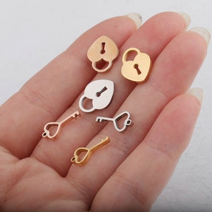 Puede incluir: Un conjunto de dijes en forma de corazón de oro y plata, con diseños de candados y llaves. Los dijes son pequeños y delicados, perfectos para agregar un toque de fantasía a joyas o manualidades.