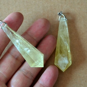 Może przedstawiać: Dwa żółte kryształowe zawieszki ze srebrnymi kółkami. Kryształy są fasetowane i mają spiczasty czubek.