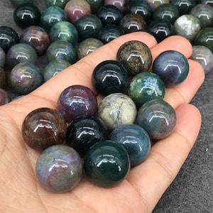 May include: A collection of green, brown, and purple agate spheres. The spheres are smooth and polished, and they have a variety of patterns and colors.