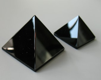 May include: Two black obsidian pyramids of different sizes. The larger pyramid is in the foreground and the smaller pyramid is in the background.