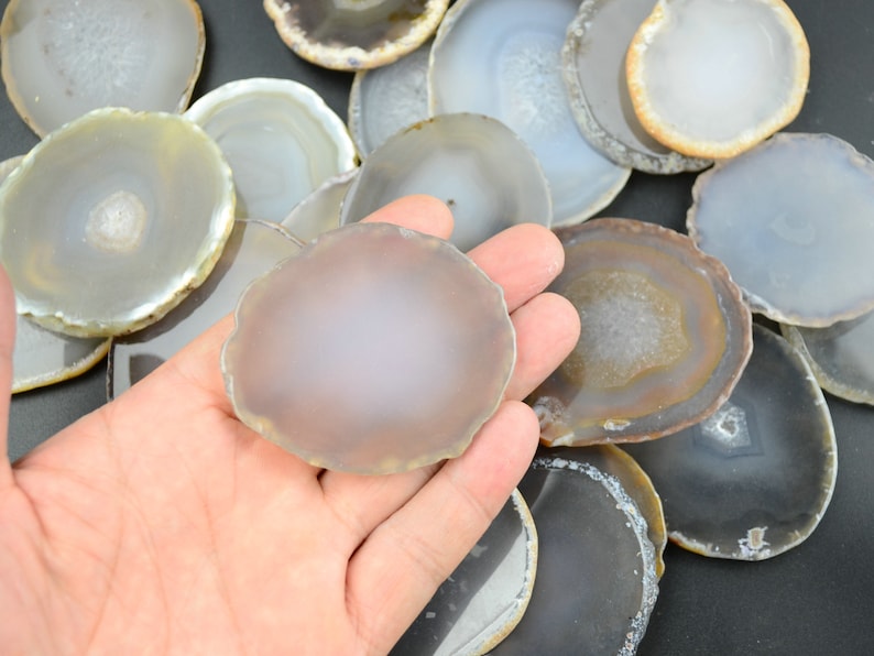 以下が含まれることがあります： 灰色と茶色の様々な色合いのアゲートのスライスを集めたものです。スライスは滑らかで磨かれており、自然で有機的な形をしています。クラフト、ジュエリー作り、または装飾的なアクセントとして使用するために最適です。
