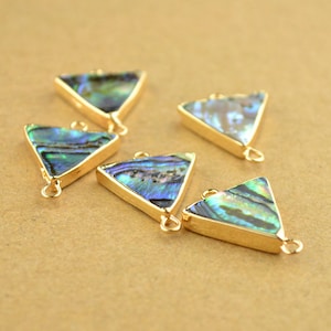 Puede incluir: Cinco colgantes de forma triangular de tono dorado con incrustaciones de nácar de abulón iridiscente. Cada colgante tiene dos anillos de salto para sujetar a las joyas.