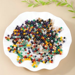 Puede incluir: Un plato blanco lleno de cuentas de piedras preciosas de varios colores. Las cuentas son pequeñas y redondas, y están dispuestas en un patrón aleatorio. Las cuentas son una mezcla de verde, azul, rojo, amarillo, marrón y negro.