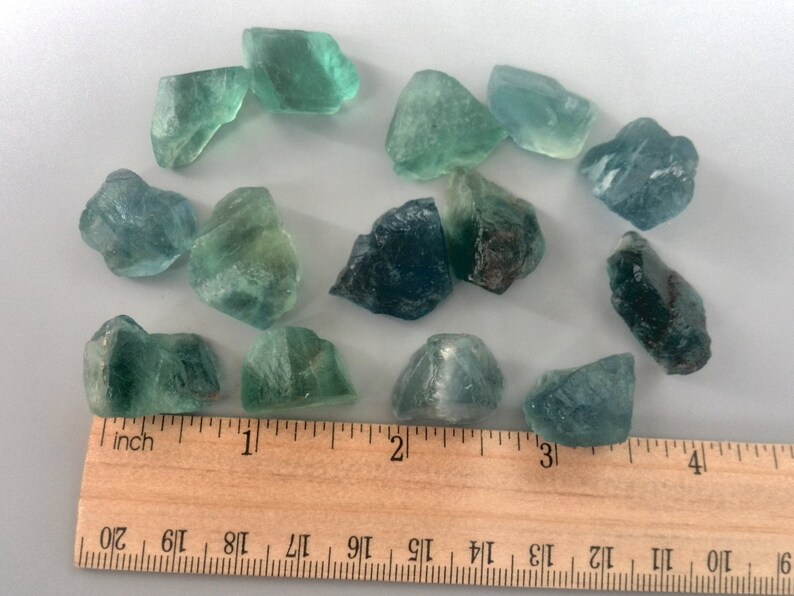 May include: A collection of 14 green and blue fluorite crystals, ranging in size from about 1/2 inch to 1 inch, displayed on a wooden ruler.