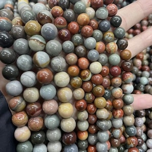 Può includere: Una collana di perline rotonde in pietre preziose multicolori. Le perline sono un mix di marrone, rosso, grigio e bianco. Le perline sono tutte più o meno della stessa dimensione e sono infilate su un filo trasparente.