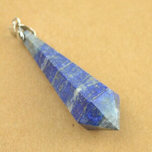 Può includere: Un ciondolo lungo e appuntito in lapislazuli con una ghiera in argento. Il ciondolo è di un blu intenso con macchie bianche e dorate.