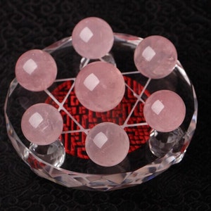 May include: Seven pink rose quartz spheres arranged in a geometric pattern on a clear crystal base.