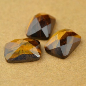 May include: Three faceted tiger's eye gemstone cabochons in a golden brown colour with a dark brown base.