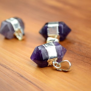 May include: Three amethyst crystal pendants with silver caps. The pendants are shaped like a pointed hexagon and have a silver loop for hanging.