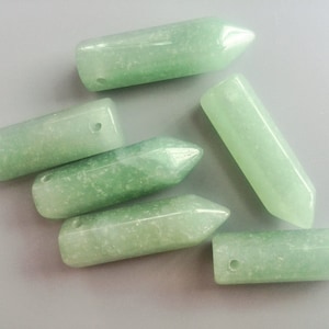 May include: Six green gemstone pendants with a pointed tip and a hole drilled through the top. The pendants are made of a light green stone with a speckled texture.