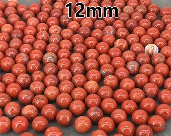 Könnte beinhalten: Eine große Gruppe von 12 mm großen roten Jaspis-Kugeln. Die Kugeln sind glatt und poliert und haben ein natürliches, erdiges Aussehen.