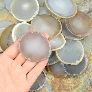 以下が含まれることがあります： 茶色、白、グレーの様々な色合いのアゲートのスライスを集めたものです。スライスは滑らかで磨かれており、自然で有機的な形をしています。スライスは積み重ねられており、一部のスライスは重なっています。