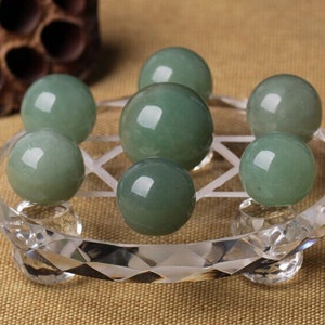May include: Seven green jade spheres arranged in a circular pattern on a clear crystal stand with a geometric design. The spheres are smooth and polished.