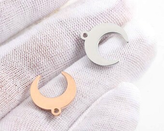 May include: Two crescent moon shaped metal charms, one silver and one rose gold. The charms have a hole at the top for attaching to jewelry.
