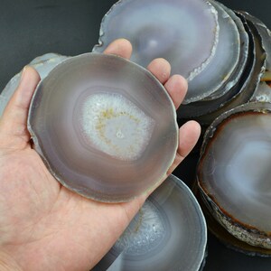 以下が含まれることがあります： グレーとブラウンの様々な色合いのアゲートコースターの積み重ね。コースターは丸型で、自然な研磨仕上げです。