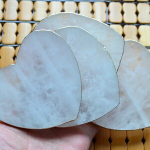 Puede incluir: Conjunto de tres posavasos blancos en forma de corazón con borde dorado. Los posavasos están hechos de piedra natural y son perfectos para proteger tus muebles de arañazos y derrames.