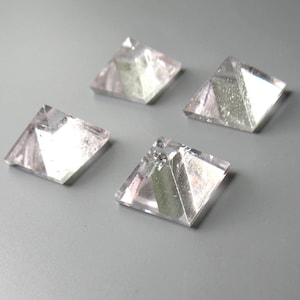 May include: Four clear quartz crystal pyramids with a green and silver inclusion. The pyramids are arranged in a square pattern on a gray surface.