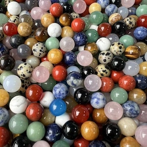 May include: A collection of smooth, polished gemstone spheres in various colors and patterns, including green, blue, red, pink, brown, and white. The spheres are arranged in a random pattern, creating a visually appealing and textured display.