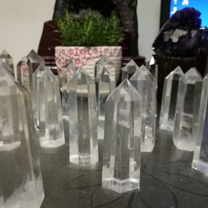 Puede incluir: Un grupo de puntas de cristal de cuarzo transparente dispuestas sobre una mesa. Los cristales son de varios tamaños y formas, algunos son más altos y delgados que otros. Todos los cristales son transparentes y tienen un ligero brillo.