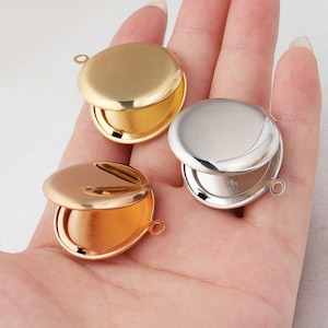 Puede incluir: Tres colgantes redondos de metal con tapa abatible. Los colgantes son de oro, plata y oro rosa.