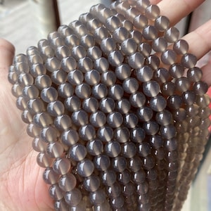 May include: A strand of grey agate beads, each bead is round and smooth. The beads are strung together on a clear thread.