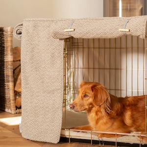 May include: A beige fabric dog crate cover with a brown and white patterned design. The cover is secured with two blue clips. A golden retriever dog is lying inside the crate.